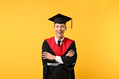 Happy student with crossed arms after graduation on orange background