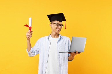 Happy student with diploma and laptop after graduation on orange background