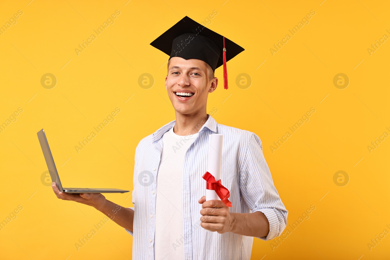 Photo of Happy student with diploma and laptop after graduation on orange background