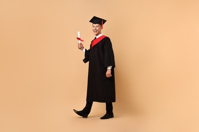 Photo of Happy student with diploma after graduation on beige background