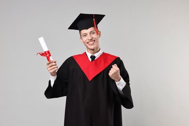 Photo of Happy student with diploma after graduation on grey background