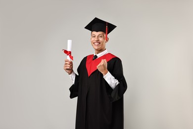 Photo of Happy student with diploma after graduation on grey background