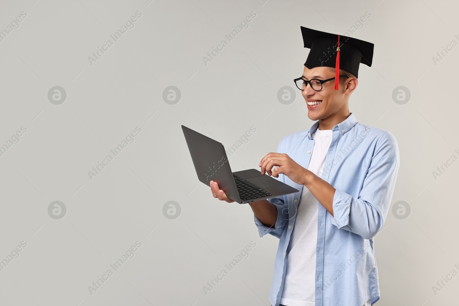 Photo of Happy student with laptop after graduation on grey background. Space for text