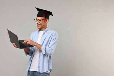 Photo of Happy student with laptop after graduation on grey background. Space for text