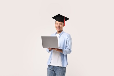 Photo of Happy student with laptop after graduation on light grey background