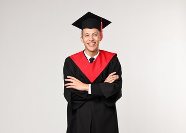 Photo of Happy student with crossed arms after graduation on light grey background