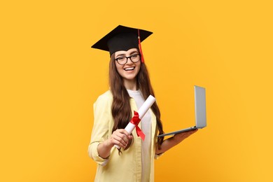 Photo of Happy student with laptop and diploma after graduation on orange background