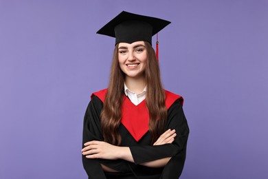 Photo of Happy student with crossed arms after graduation on violet background