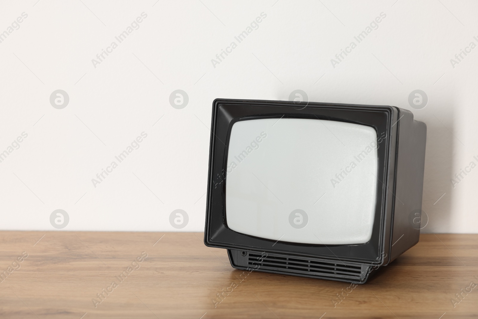 Photo of Retro tv set on wooden shelf against white wall. Space for text