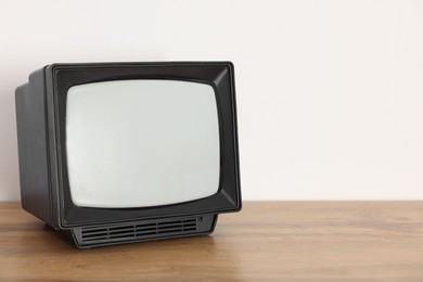 Photo of Retro tv set on wooden shelf against white wall. Space for text