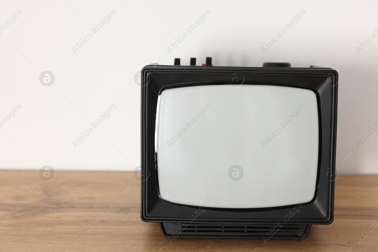 Photo of Retro tv set on wooden shelf against white wall. Space for text