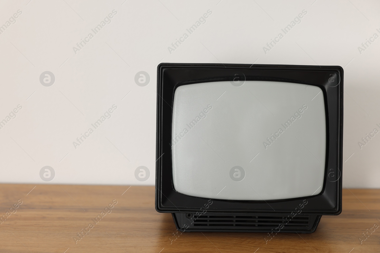 Photo of Retro tv set on wooden shelf against white wall. Space for text