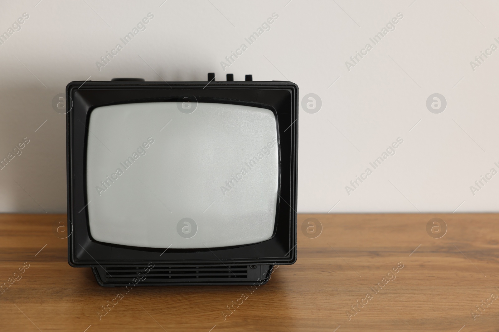 Photo of Retro tv set on wooden shelf against white wall. Space for text