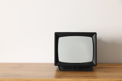 Photo of Retro tv set on wooden shelf against white wall. Space for text