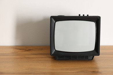 Photo of Retro tv set on wooden shelf against white wall. Space for text