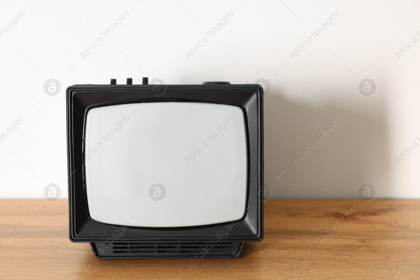 Photo of Retro tv set on wooden shelf against white wall. Space for text