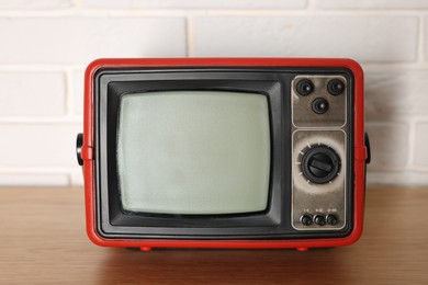 Photo of Retro tv set on wooden shelf against white brick wall