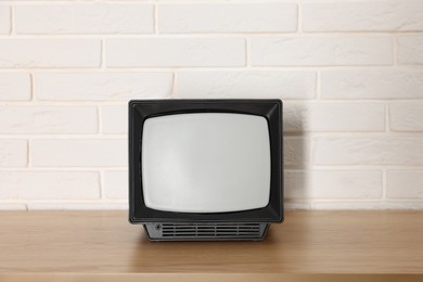 Photo of Retro tv set on wooden shelf against white brick wall