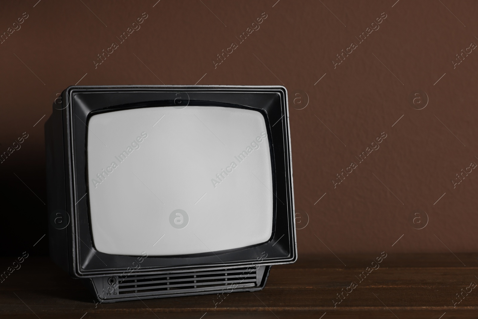 Photo of Retro tv set on wooden shelf against brown wall. Space for text