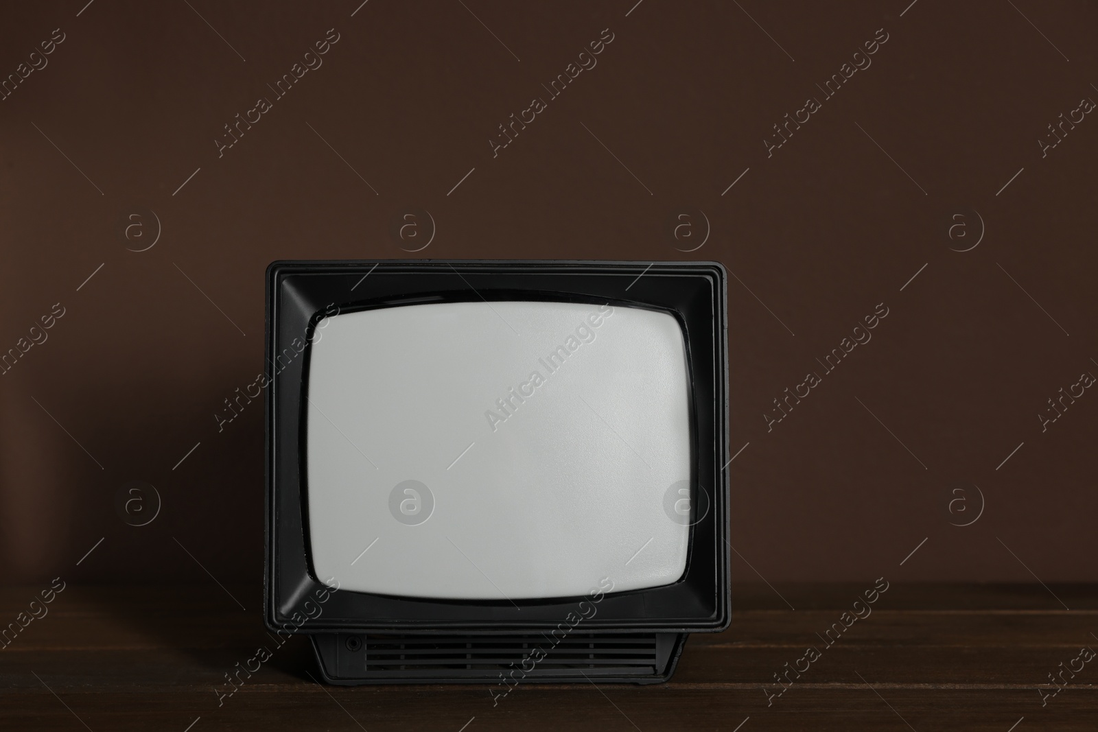 Photo of Retro tv set on wooden shelf against brown wall