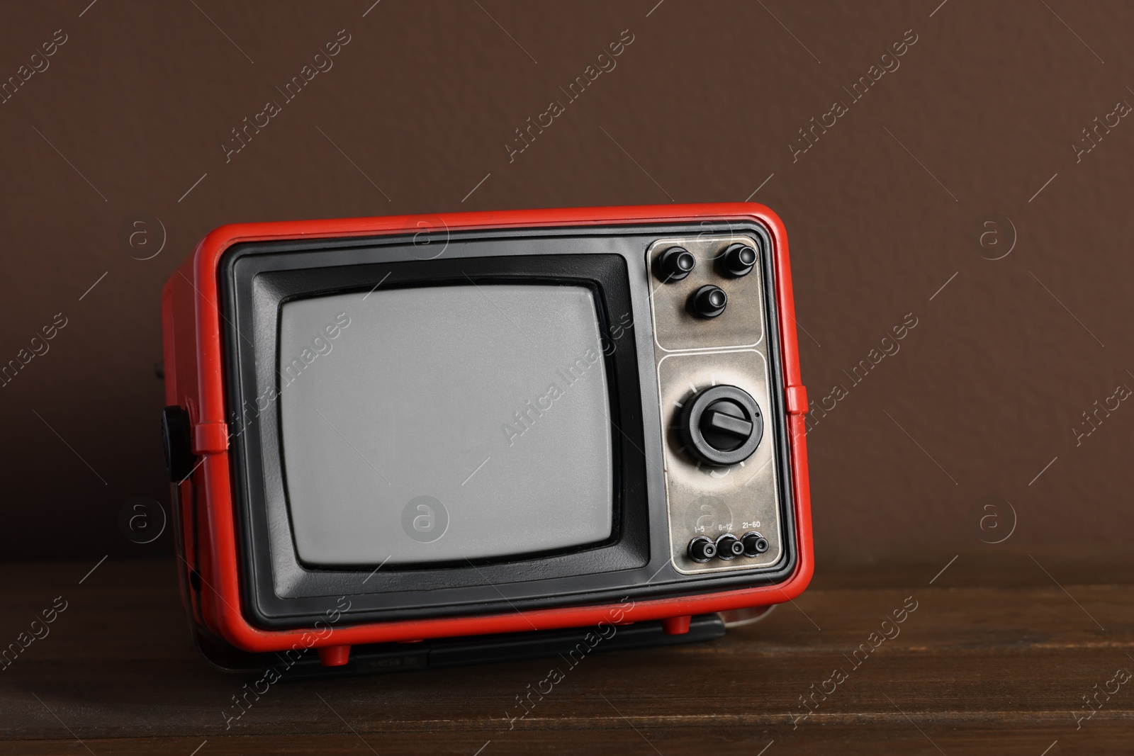 Photo of Retro tv set on wooden shelf against brown wall