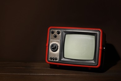 Photo of Retro tv set on wooden shelf against brown wall. Space for text