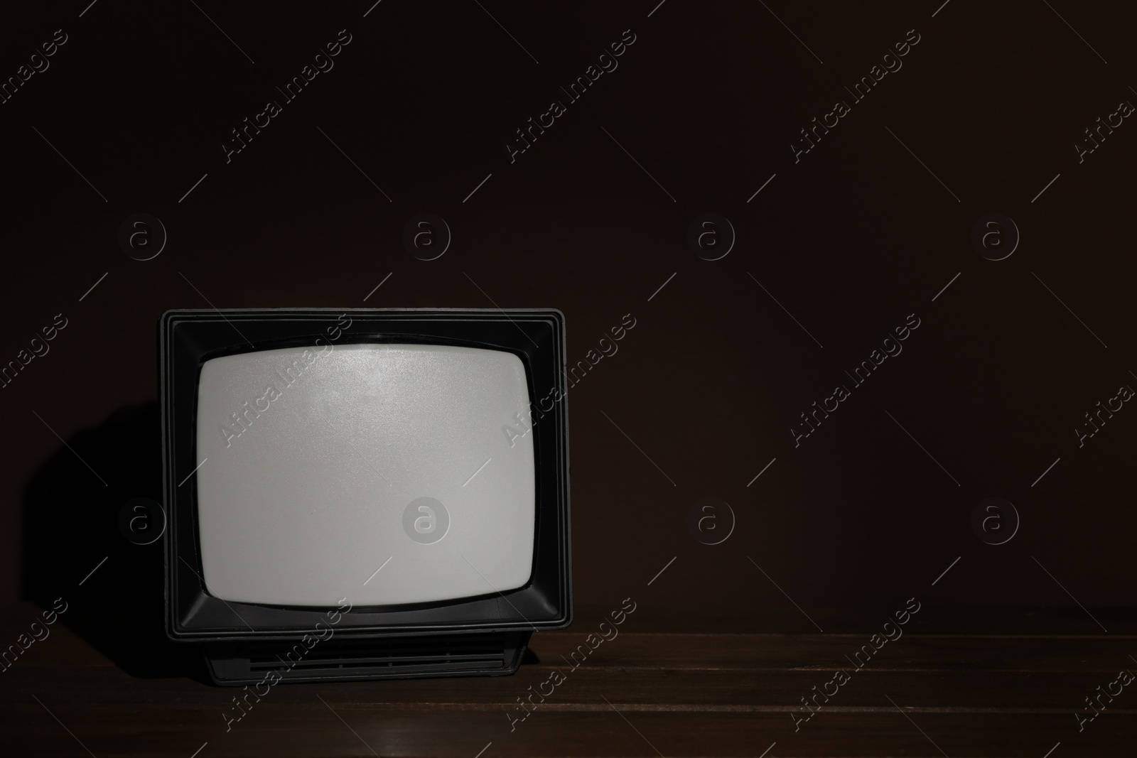 Photo of Retro tv set on wooden shelf against dark background. Space for text