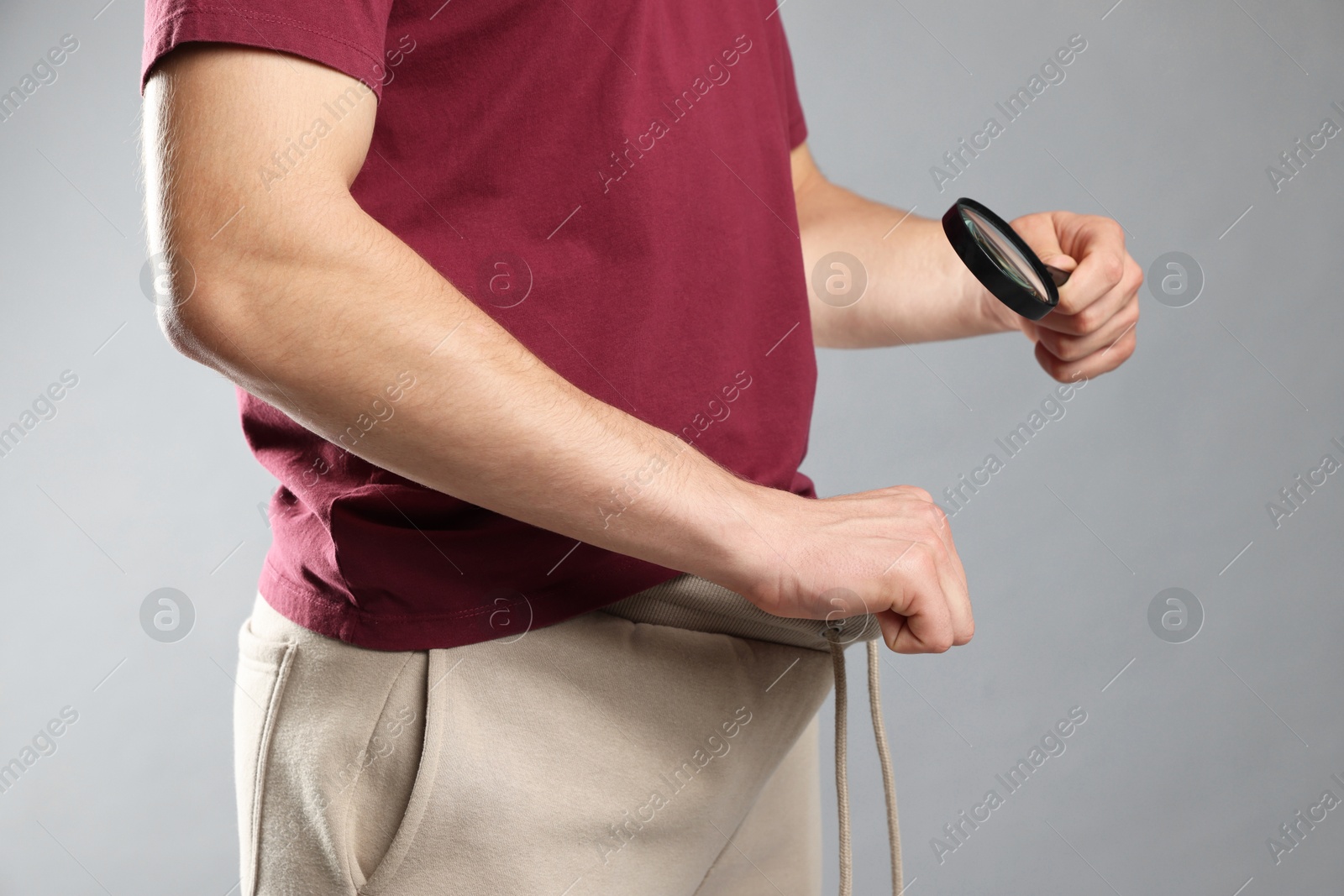 Photo of STD (sexually transmitted diseases). Man examining intimate area with magnifying glass on grey background, closeup