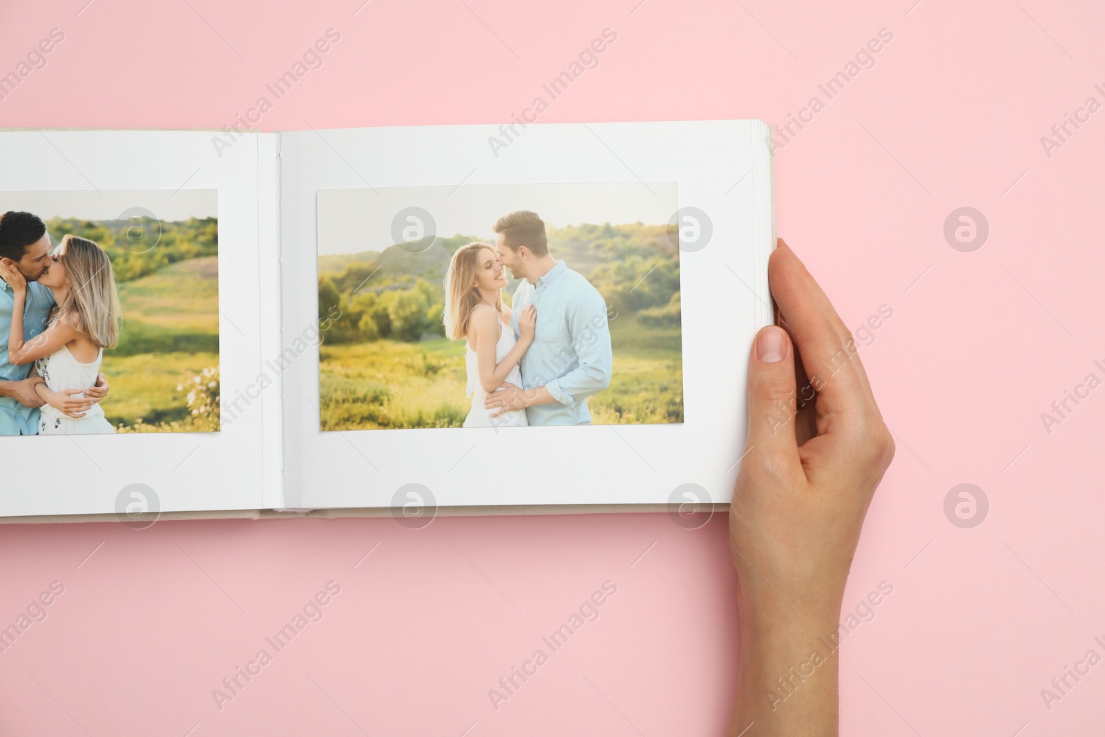 Photo of Woman looking at photos in photo album on pink background, top view