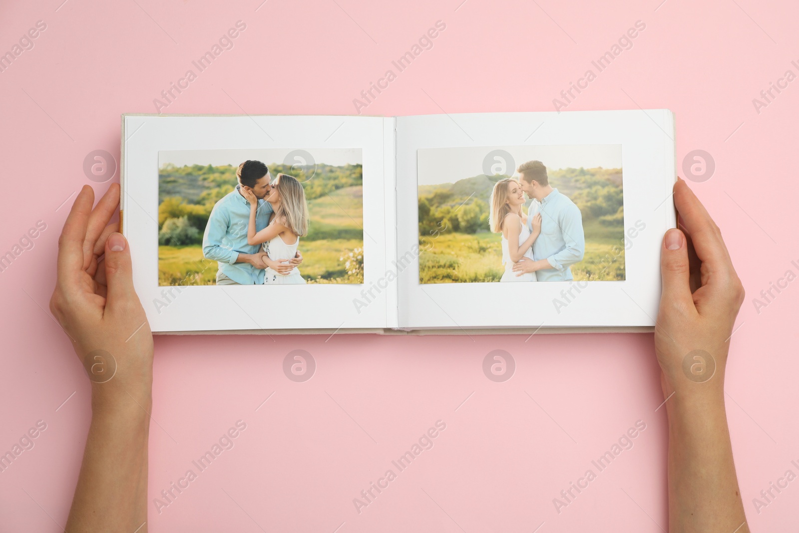 Photo of Woman looking at photos in photo album on pink background, top view