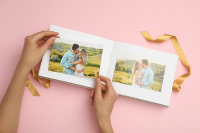 Photo of Woman looking at photos in photo album on pink background, top view