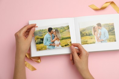 Photo of Woman looking at photos in photo album on pink background, top view