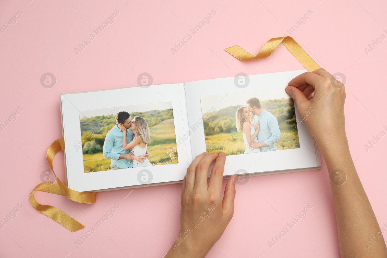 Photo of Woman looking at family photos in photo album on pink background, top view