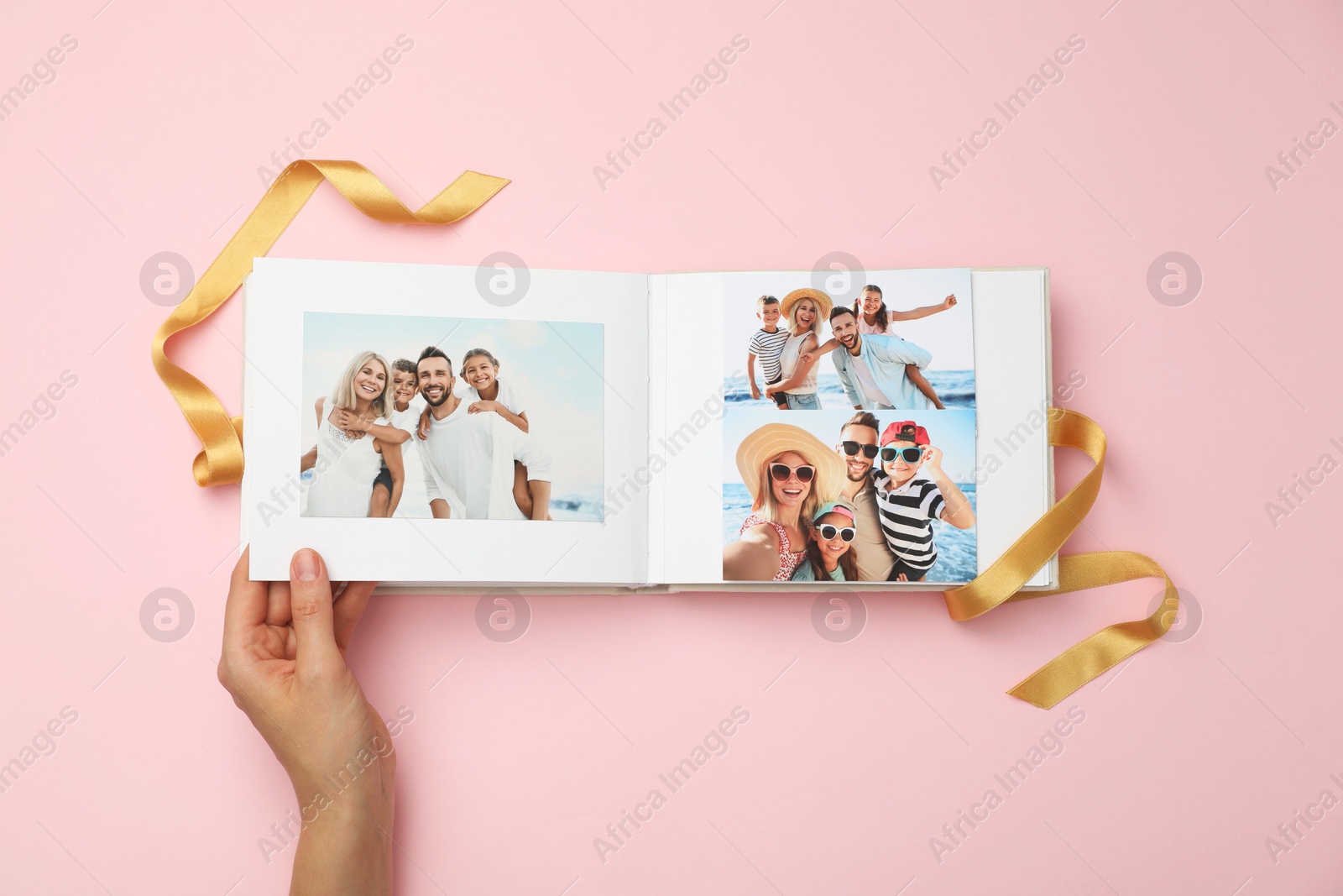 Photo of Woman looking at family photos in photo album on pink background, top view