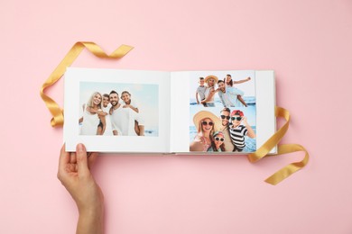 Woman looking at family photos in photo album on pink background, top view