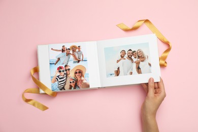 Photo of Woman looking at family photos in photo album on pink background, top view