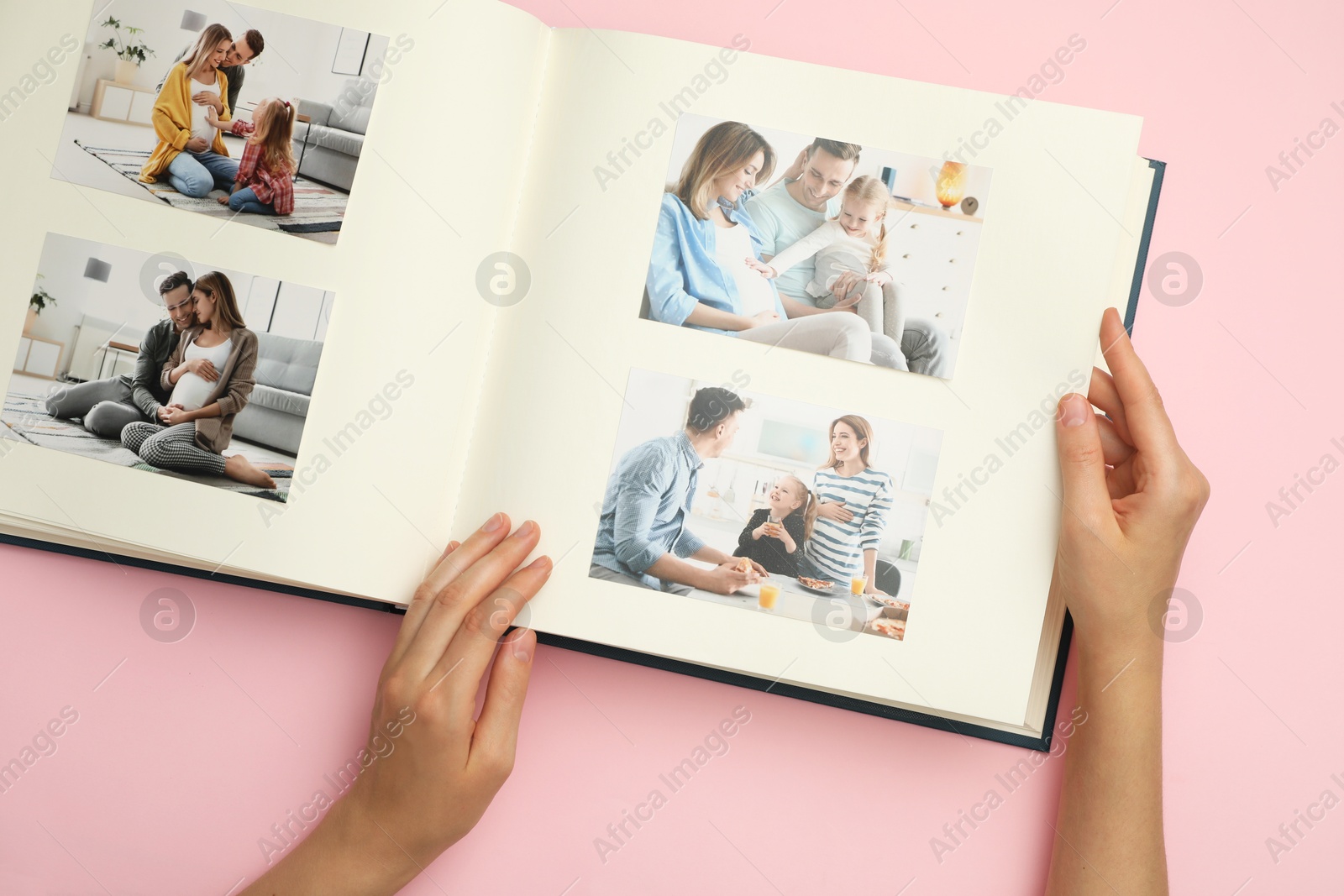 Photo of Woman looking at family photos in photo album on pink background, top view