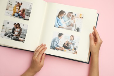 Photo of Woman looking at family photos in photo album on pink background, top view