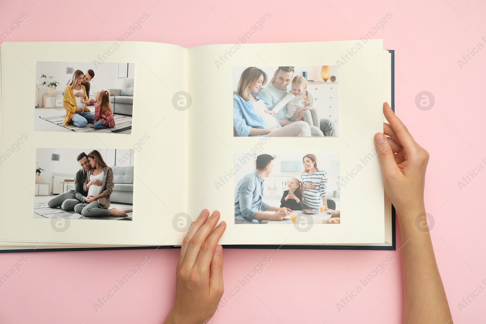 Photo of Woman looking at family photos in photo album on pink background, top view