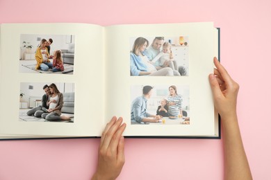 Photo of Woman looking at family photos in photo album on pink background, top view