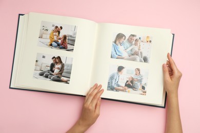 Photo of Woman looking at family photos in photo album on pink background, top view