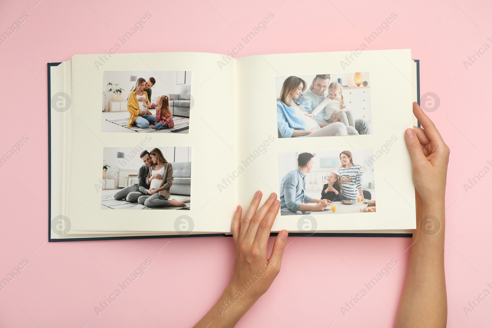 Photo of Woman looking at family photos in photo album on pink background, top view