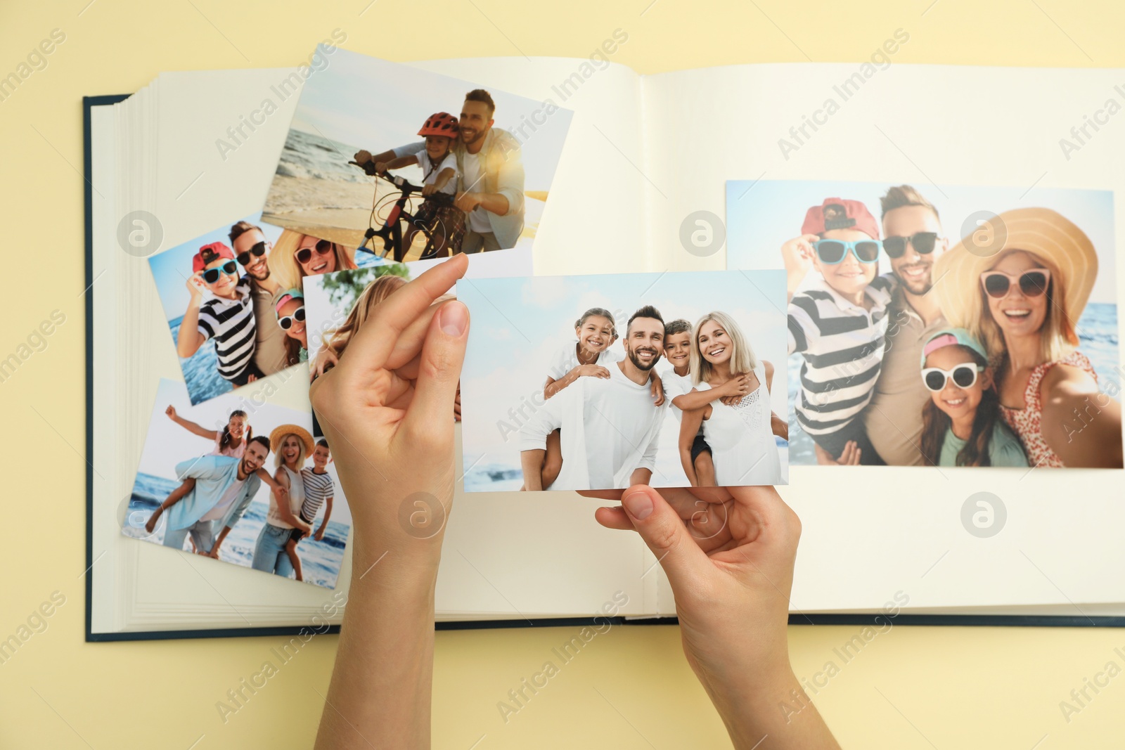 Photo of Woman with open photo album and different photos on beige background, top view