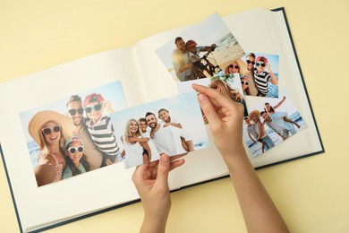 Photo of Woman with open photo album and different photos on beige background, top view