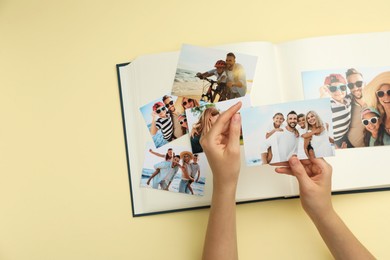 Photo of Woman with open photo album and different photos on beige background, top view