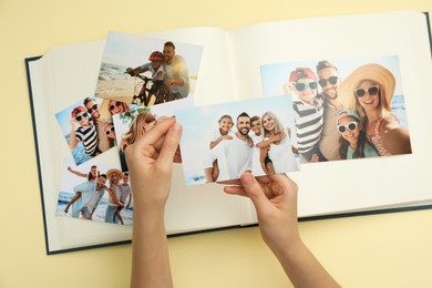 Woman with open photo album and different photos on beige background, top view