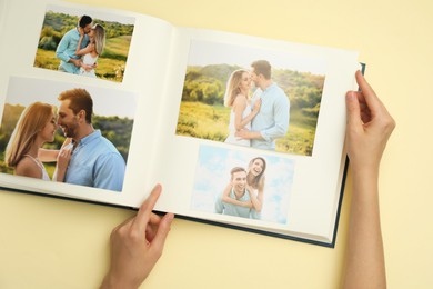 Woman looking at family photos in photo album on beige background, top view