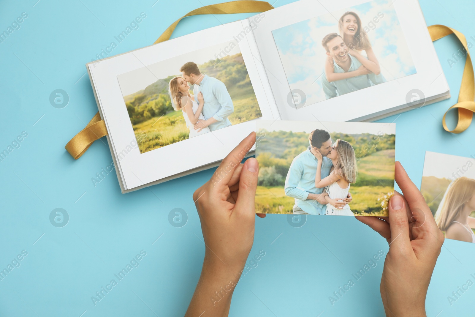 Photo of Woman with open photo album and different photos on light blue background, top view