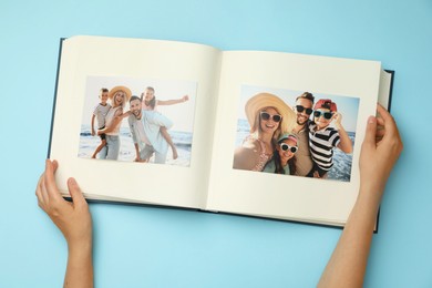 Photo of Woman looking at family photos in photo album on light blue background, top view