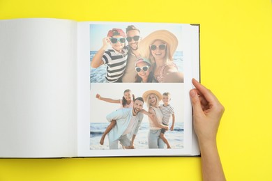 Woman looking at family photos in photo album on yellow background, top view